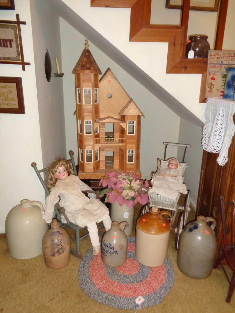 A small corner of a room staged with a wooden house antique jugs and antique dolls